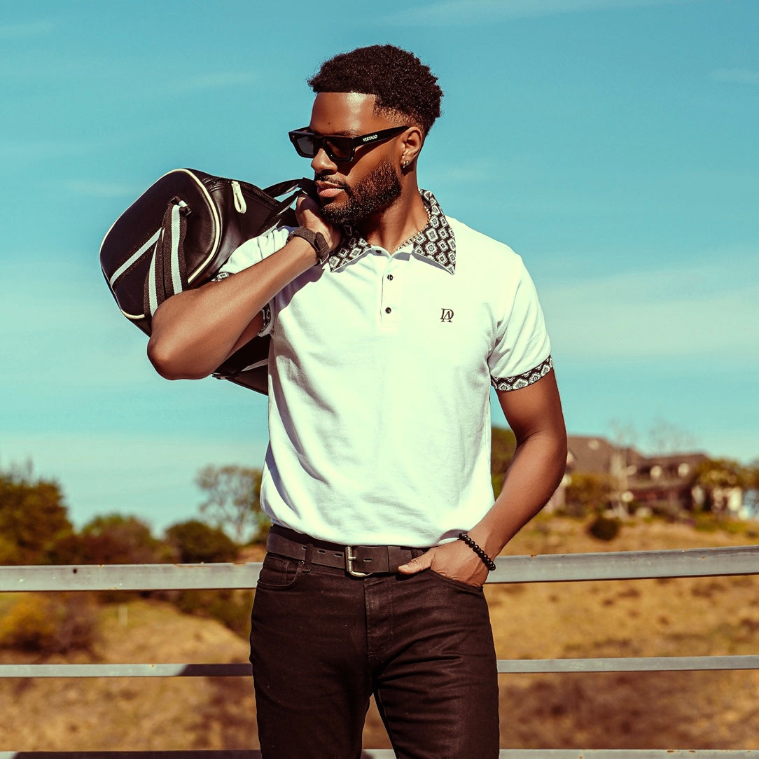 Man holding a golf bag outdoors with a clear sky background wearing alan daniel meso polo