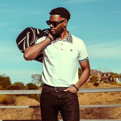 Man holding a golf bag outdoors with a clear sky background wearing alan daniel meso polo